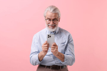 Wall Mural - Portrait of stylish grandpa with glasses using smartphone on pink background