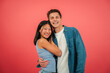 © Jose Calsina - Young adult multiracial couple smiling and hugging in front of a red color studio background. Two people in a romantic and happy pose looking at the camera together. Lovely boyfriend and girlfriend