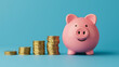 © Janjira - A pink piggy bank next to stacks of gold coins on a blue background, symbolizing savings, investment, and financial growth.