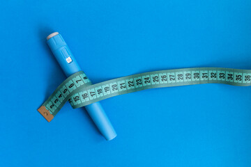 Blue injector dosing pen for subcutaneous injection of antidiabetic medication, anti-obesity medication on a blue background. Measuring tape around the injector.  Drug and weight loss