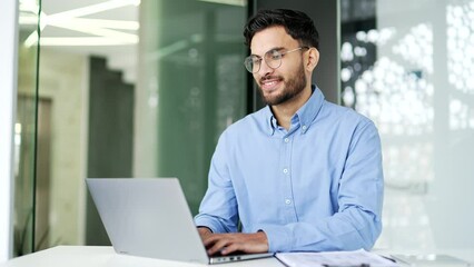 Worker in glasses working typing on a laptop sitting at a workplace in business office. Happy man employee using computer application, banking, texting a client, chatting online. busy with a project