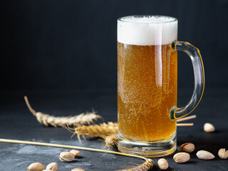 Wall Mural - Mug of cold beer on a dark table, wheat ears and pistachios