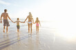 © peopleimages.com - Support, walking and family holding hands at a beach for summer, fun and bonding at sunset together. Travel, care and back of children with parents at sea for vacation, holiday or tropical adventure
