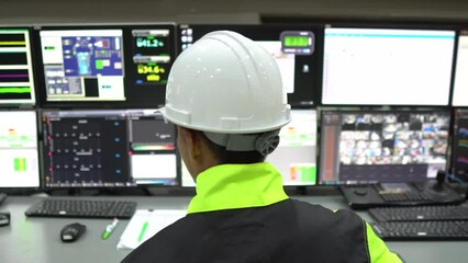engineer working in a control room,programming to manage industrial machines,monitoring multiple scr