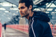 © BullRun - Motivated fit man dressed in stylish active clothes listening music payer in earphones and doing warming up before run.Athletic male jogger doing stretching on bridge before workout