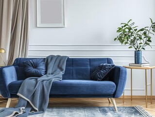 Wall Mural - A blue couch with a blue blanket draped over it sits in a room with a white wall. A potted plant sits on a table next to the couch