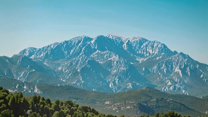 Poster - A breathtaking view of a majestic mountain range with lush trees in the foreground, set against a clear blue sky, A majestic mountain range under a clear blue sky