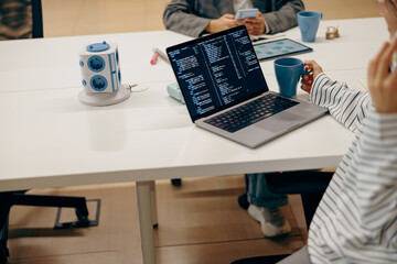 Close up of female software engineer writing code on laptop with screens setup in coworking 