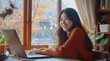 © yj - A smiling korean young woman sitting at her desk, working on her laptop in a home office room with a window. a calm and tranquil mood for working. generative AI