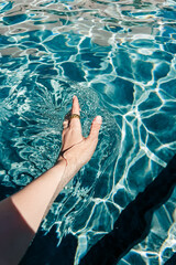 Hand touching pool surface with sun ripple on the water