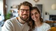 © olga_demina - Young couple with glasses smiling in their new living room. Represents new beginnings, home ownership, and modern lifestyle.