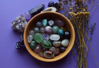 Wall Mural - Beautiful natural semi-precious stones in a wooden plate and dry herbs on a purple background. Predictions, witchcraft, spiritual esoteric practice.