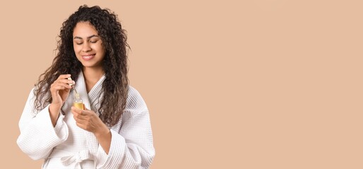 Canvas Print - Happy African-American woman with healthy curly hair and serum on beige background with space for text