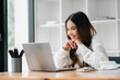 © Mongta Studio - A woman is sitting at a desk with a laptop open in front of her. She is smiling and she is enjoying her work