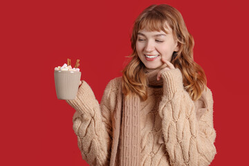 Canvas Print - Pretty young woman holding cup of hot chocolate with marshmallows and cinnamon on red background