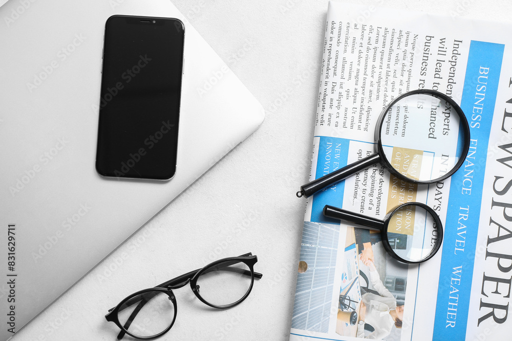 Newspaper with magnifying glasses, laptop and mobile phone on white background
