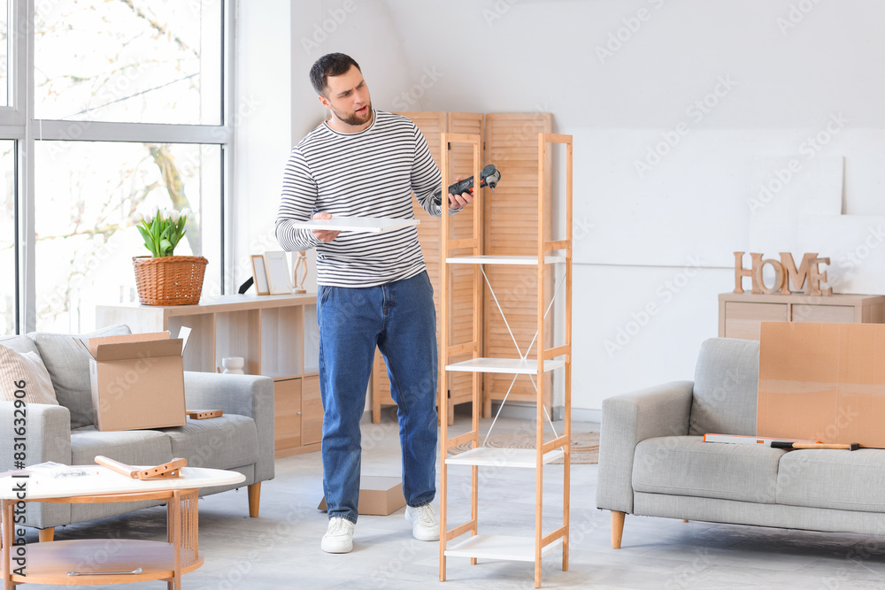 Troubled young man with drill assembling shelf unit at home
