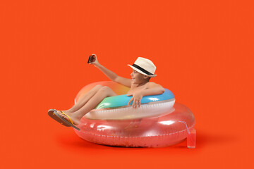 Poster - African-American little boy in shorts, hat with mobile phone and inflatable rings taking selfie on orange background