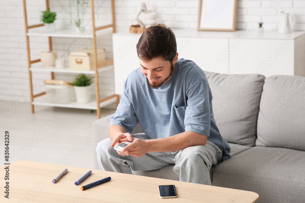 Diabetic young man using glucometer on sofa at home