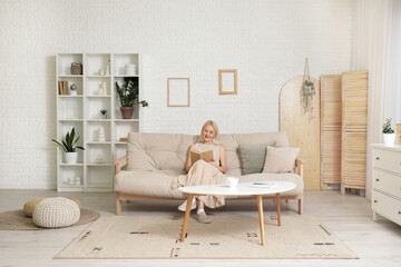 Sticker - Mature woman reading book on sofa at home