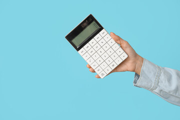 Wall Mural - Female hand with calculator on blue background