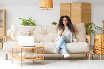 Sticker - Young African-American woman on sofa watching TV at home