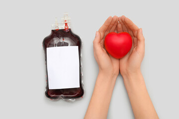 Wall Mural - Female hands with heart and blood pack for transfusion on grey background
