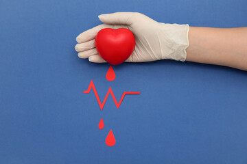 Wall Mural - Female hand in rubber glove with grip ball, paper blood drops and cardiogram sign on blue background. Donation blood concept.