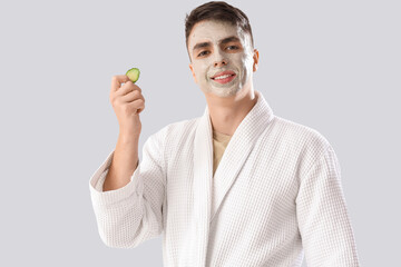 Poster - Young man with applied clay mask and cucumber slice on light background