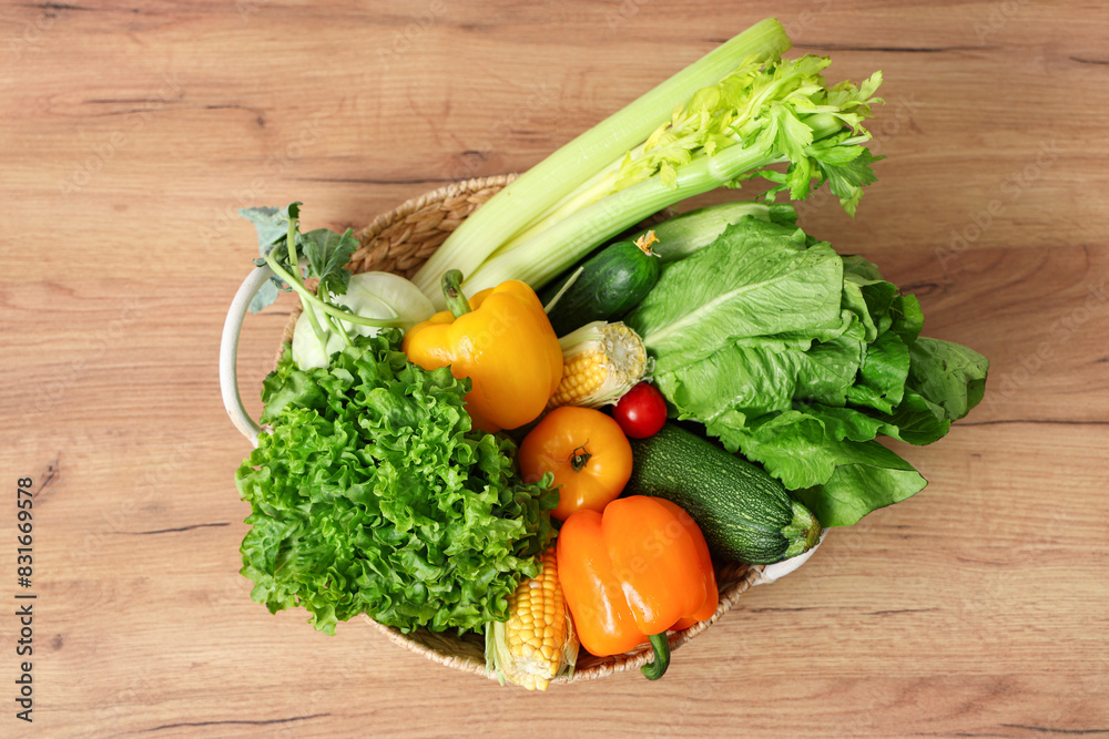 Wicker basket with different fresh vegetables on wooden kitchen counter, top view