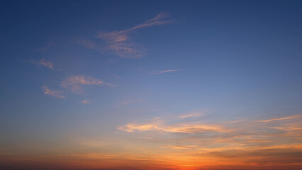 Wall Mural - A tranquil sunrise with a gradient sky transitioning from deep blue at the top to warm orange and yellow hues near the horizon, highlighted by soft, wispy clouds. Cloud background. 
