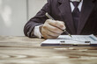 © NanSan - A businessman in a formal suit signs a contract, hands close up, highlighting financial terms like amortization, APR, and asset management, documents symbolizing various loan and insurance concepts.