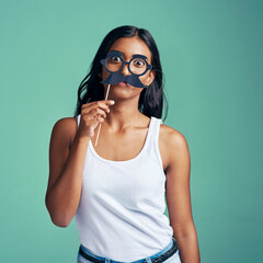 Sticker - Woman, studio and party prop on face, surprised and comic with holding mask for humorous or comedy. Photo booth, portrait and green background, silly and creative fun with Indian female person