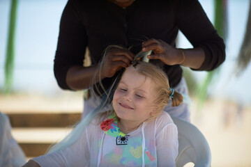 holding braids with pink color on little kid head. stylist applying braiding hair on young baby.