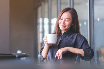 Wall Mural - Portrait image of a beautiful young asian woman holding and drinking hot coffee in cafe