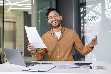 Poster - Happy businessman celebrating success at the desk with paperwork in a modern office