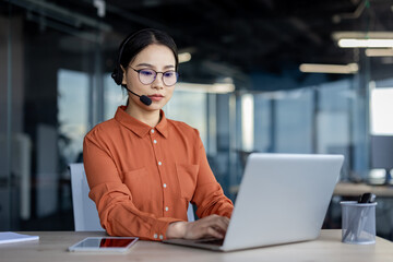 Call center agent wearing a headset while working diligently on a laptop at a modern office desk. Professional work environment.