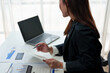 © crizzystudio - Asian businesswoman working in office with documents and laptop Documents of the worker calculating financial indicators, smiling happily at the success and results of work.