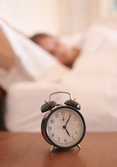 Sleeping, woman and closeup of alarm clock in bedroom with time for wake up, morning and snooze for wellness. Relax, dreaming and tired girl and watch with noise alert for late and lazy in apartment