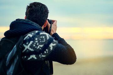 Beach, man and camera photography at sunset on holiday, travel or summer vacation in Spain. Dslr picture, back view or person at ocean outdoor for tourism, adventure or journey in nature by sea water