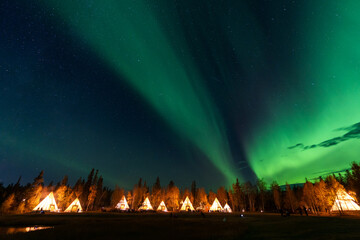 Wall Mural - Amazing northern lights dancing over the light up Tipi or Tepees at Aurora Village in Yellowknife, Northwest Territories, Canada.