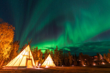 Wall Mural - Amazing northern lights dancing over the light up Tipi or Tepees at Aurora Village in Yellowknife, Northwest Territories, Canada.