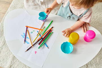 Wall Mural - A little girl is happily playing with colored crayons on a table as part of a Montessori educational activity at home.