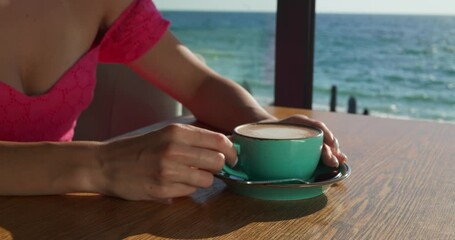 Wall Mural - Woman with cup of coffee at table in cafe near sea, closeup. Camera moving around