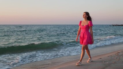 Wall Mural - Pretty woman walking on beach by sea at sunset. Camera moving with girl