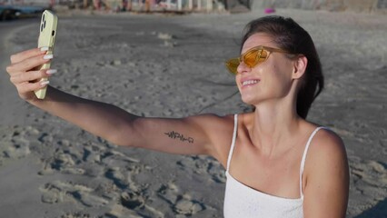 Wall Mural - Beautiful woman in bright sunglasses taking selfie on   beach. Camera moving right