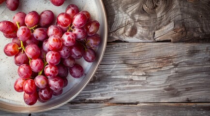 Wall Mural - Plate with bunch of red grapes on a wooden table, top view.