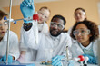 © AnnaStills - Selective focus shot of young Black teacher and group of ethnically diverse kids doing laboratory experiment in Chemistry class