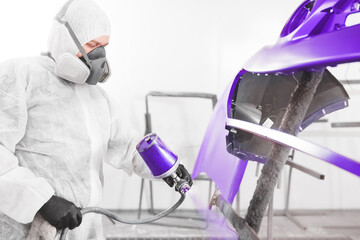 Wall Mural - Auto mechanic worker painting car bumper with spray gun in a paint chamber during repair work.