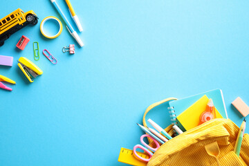 Back to school concept with school supplies scattered on a vibrant blue background. The image features a yellow backpack, notebooks, pens, pencils, scissors, rulers, and various colorful clips